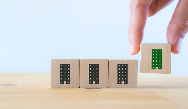 Green and eco building concept. LEED certification. Leadership in Energy and Environmental Design. Sustainable building. Hand holds the wooden cubes with green building symbols on white background.