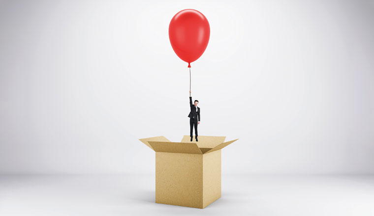 Abstract image of young european businessman flying on red balloon out of paper box on light background. Success, business and happiness concept