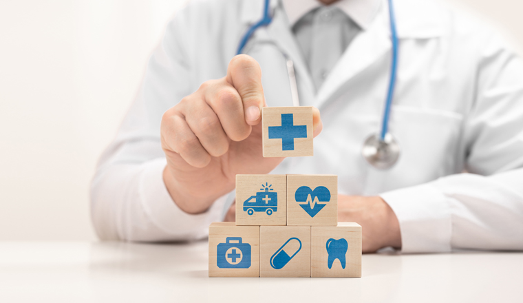 Doctor hand choose cross sign on wood cube block. healthcare medical icon on wooden blocks stacked in pyramid shape. doctor in white coat arranging cubes with medical symbols in pyramid on desk.banner