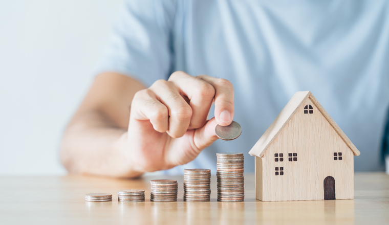 Man hand put coin on coins stack with wooden house on wood table. saving money for buying house, financial plan home loan concept.