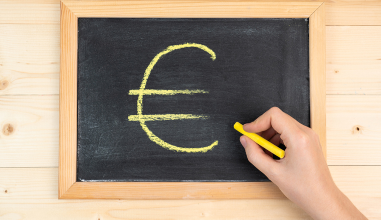 A woman's hand draws the euro symbol in yellow chalk on a black blackboard in a frame