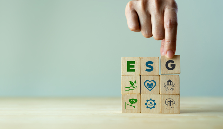 ESG concept of environmental, social and governance. Sustainable corporation development. Hand holds wooden cubes with abbreviation ESG standing with other ESG icons on grey background. Copy space.