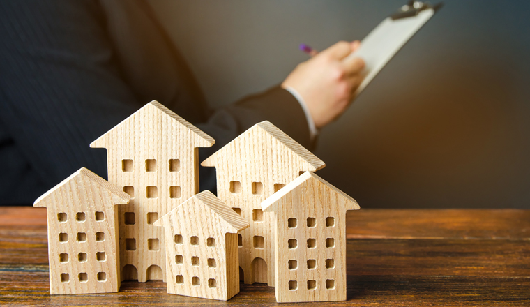 Wooden houses and a businessman in the background. Real estate market analysis concept. Affordable housing, rental apartments and houses. Mortgage rates. Realtor services.