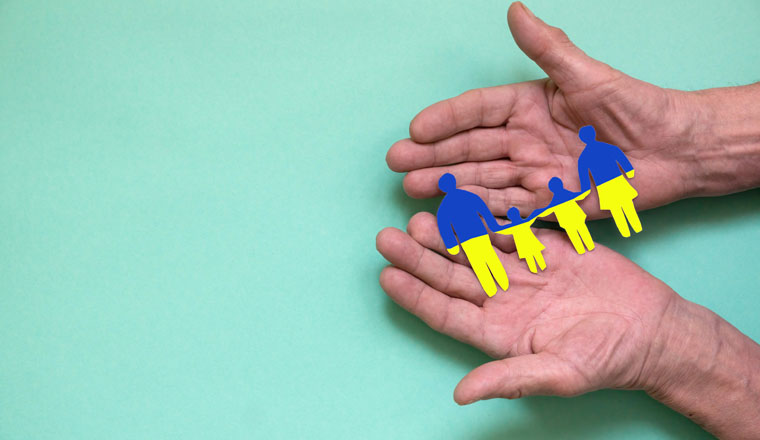 The concept of an old man wishes peace in the family of Ukraine. The hands of an elderly person hold a paper-cut family painted in the national colors of Ukraine. copyspace on the left. Ukrainian flag