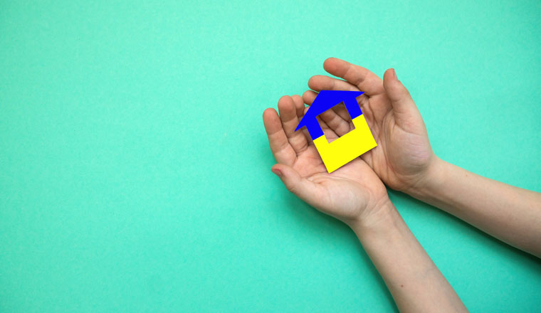 A house cut out of paper painted in the colors of the Ukrainian flag in the hands of a child. The child is holding a paper house. Ukrainian flag. There is a copyspace