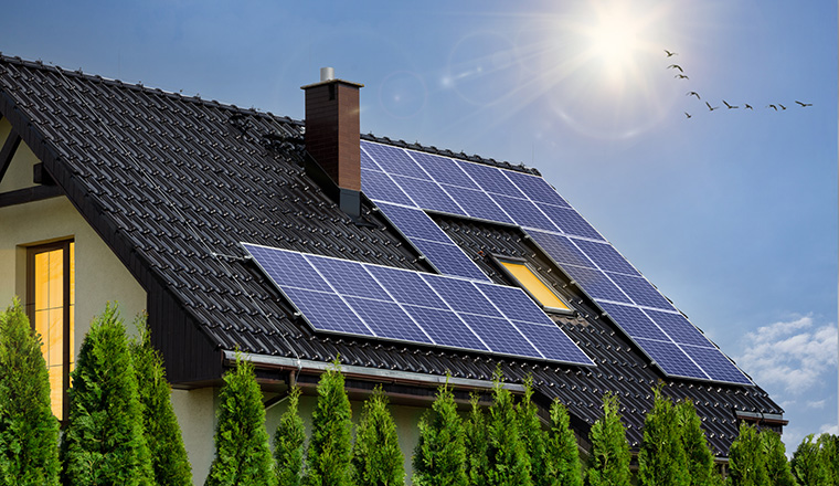 Modern house with solar panels on roof. Photovoltaic panels on roof. Light in windows, green energy concept.