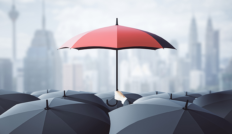 Businessman hand holding red umbrella over crowd on blurry dull city background. Risk, protection and safety concept