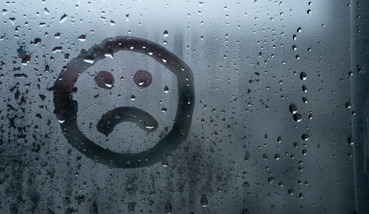 Sad smiley drawn by hand on wet fogged glass from the rain, copy the space. Concept of loneliness, sadness, bad weather