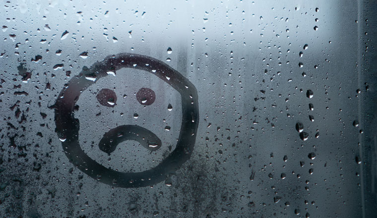 Sad smiley drawn by hand on wet fogged glass from the rain, copy the space. Concept of loneliness, sadness, bad weather