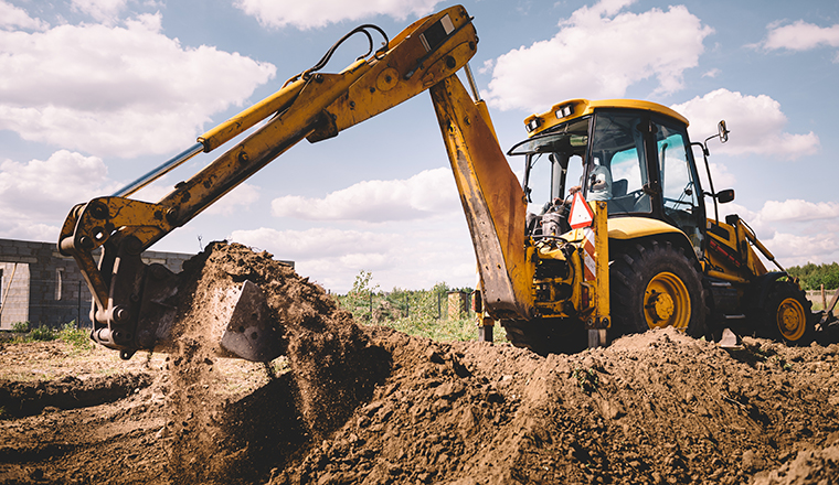 Excavator working at house construction site - digging foundations for modern house. Beginning of house building. Earth moving and foundation preparation.