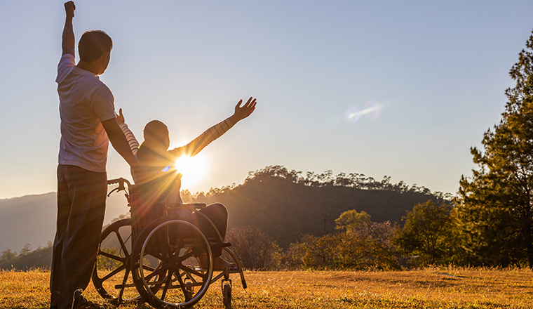 Silhouette of joyful couple in wheelchair raised hands at sunset