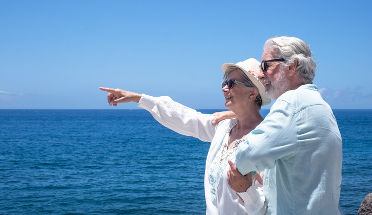 Attractive caucasian senior couple hugging in front to the sea looking at horizon over water. Two retired people enjoying summer and vacation