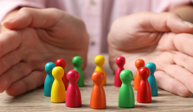 Woman protecting colorful pawns at wooden table, closeup. Diversity and Inclusion concept