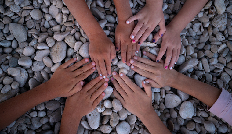 Overhead view of hands of four children making a circle on a pebble beach. Conceptual of childhood and friendship.