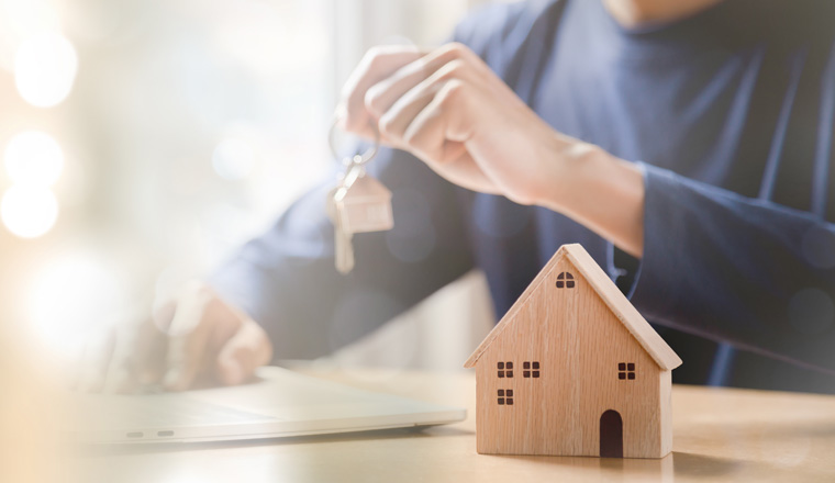 Businessman choosing mini wood house model from model and row of coin money on wood table, selective focus, Planning to buy property. Choose what's the best. A symbol for construction ,ecology, loan concepts.