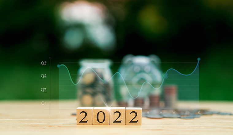 Text "2022" on wooden block on wood table, green background. Blur stack coin,coin in jar, piggy bank, graph. Savings plans for housing, business growth, loan, investment, financial concept.