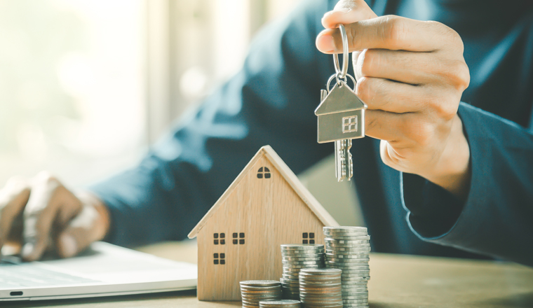 Businessman choosing mini wood house model from model and row of coin money on wood table, selective focus, Planning to buy property. Choose what's the best. A symbol for construction ,ecology, loan concepts.