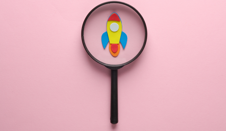 Space rocket with a magnifying glass on a pink background. Business concept