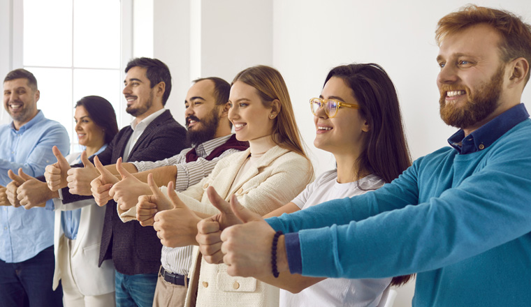 Multiracial group of happy business people showing thumbs up all together. Cheerful male and female employees standing in office, giving thumbs up and smiling. Dream team, teamwork, success concept