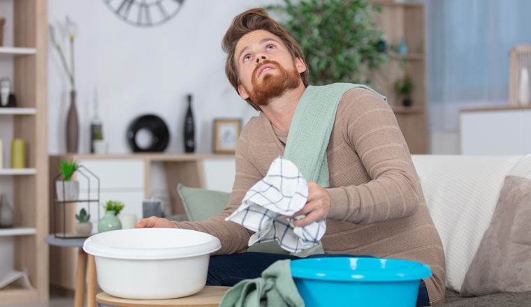 man collecting water in bucket from ceiling