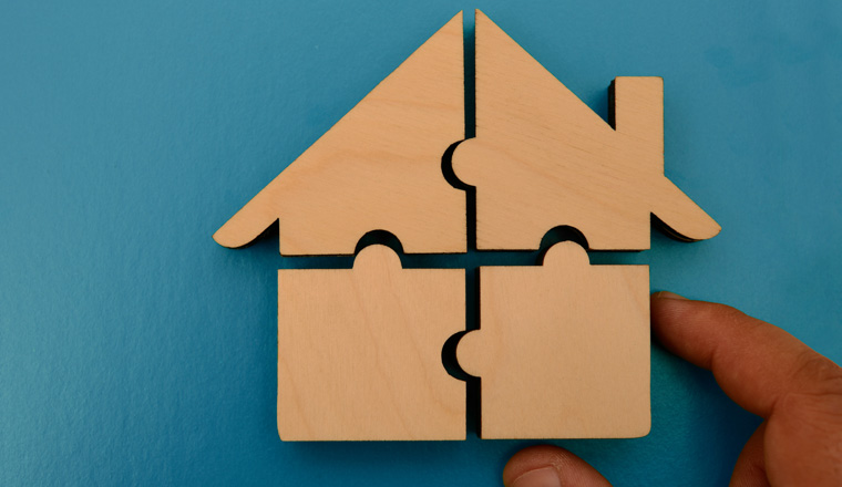 hand holds pieces of white wooden house puzzle isolated on blue background. wooden home made from natural material of jigsaw. puzzle in the form of wood house. for sale or rent. concept of mortgage
