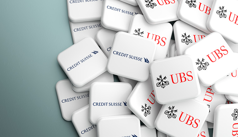 Logos of Credit Suisse and UBS Bank on a heap on a table. Concept for a possible merger or take over. Copy space. Web banner format.