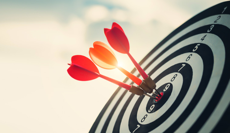 Close up shot of the dart arrow hit on bulleyes of dartboard to represent that the business reached the target  with dark tone picture style. Target and goal as concept.