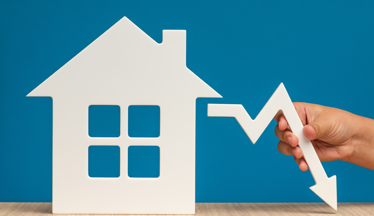 The collapse in real estate prices. Sale in the housing market. Reducing the value of real estate. Model of a house on a blue background and hand holding a white graph arrow pointing down