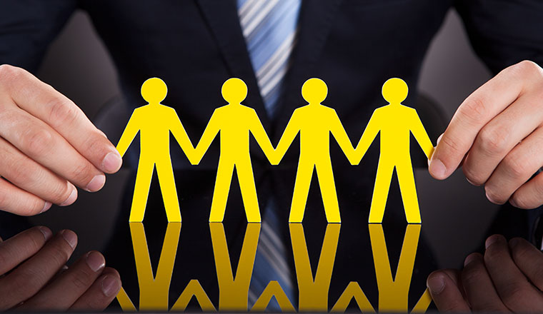 Midsection of businessman's hands holding paper people chain on desk against black background