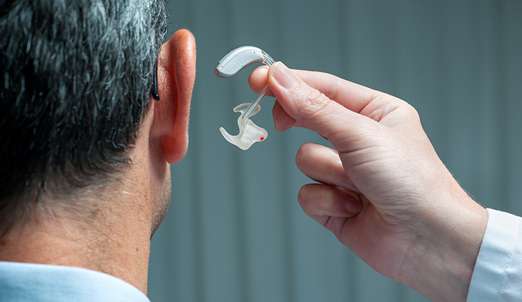 Doctor inserting hearing aid in senior's ear