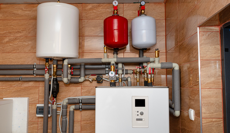 A modern air heat pump installed in the home's boiler room, visible plastic pipes and valves.