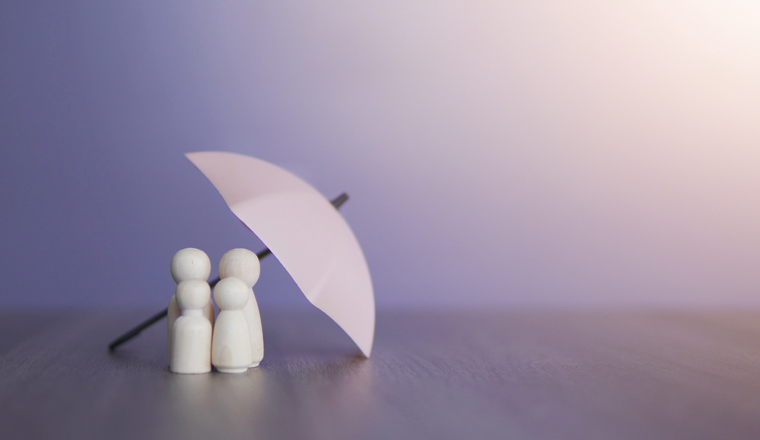 Umbrella and wooden dolls with copy space. Family protection and insurance coverage concept.