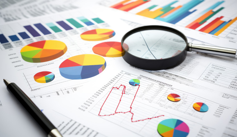 Printed business documents with colorful charts and graphs being analyzed through a magnifying glass