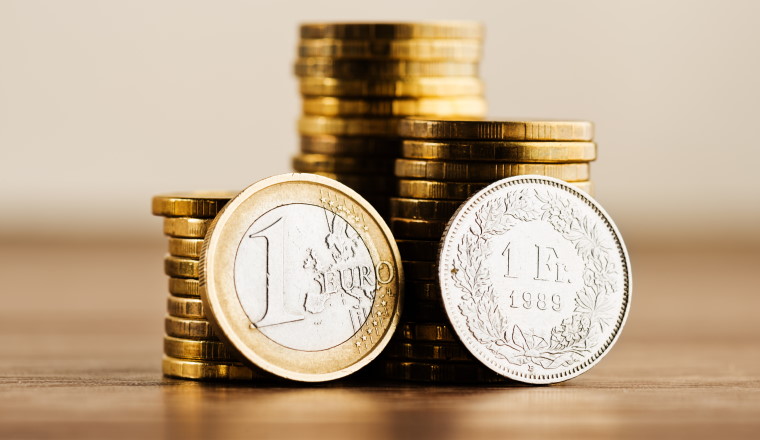 one euro coin and one swiss frank and gold money on the desk