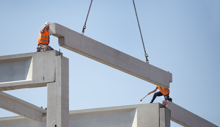 Construction workers standing on concrete beam on height and placing truss lifted by crane