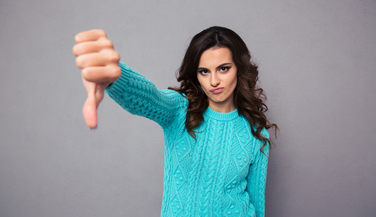 Portrait of a young woman showing thumb down over gray background