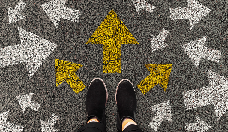 Person standing on road with arrow markings pointing in different directions or pathway, decision making concept. Top view.