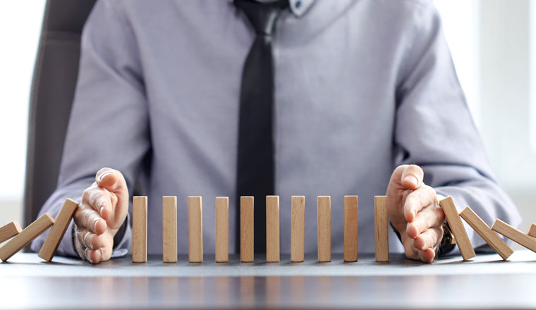 business man blocks falling blocks with his hands to prevent domino effect