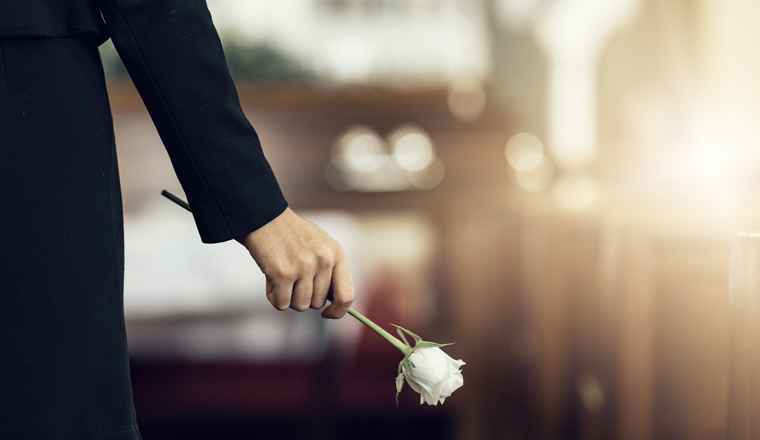 Flower, funeral and hand holding rose in mourning at death ceremony with grief for loss burial. Floral, church or cemetary with person holding plant for sad bereavement or cemetary event in a chapel.