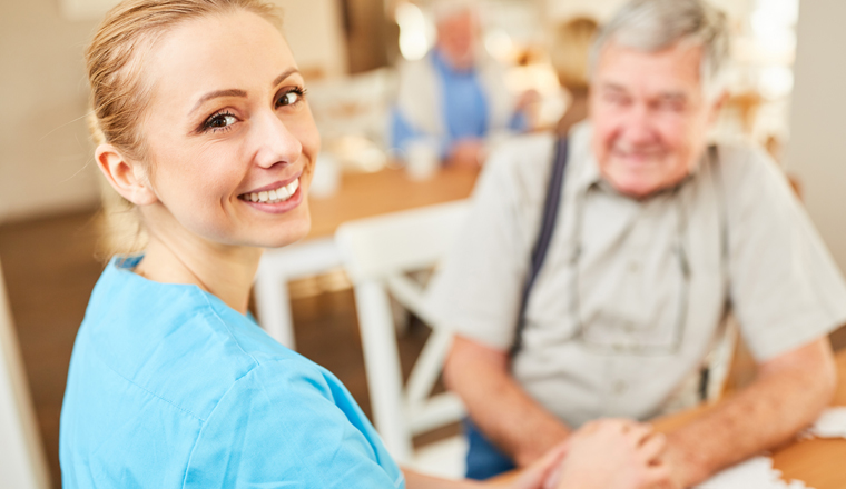 Lächelnde Pflegehilfe Frau oder Altenpfleger tröstet einen Senior im betreuten Wohnen