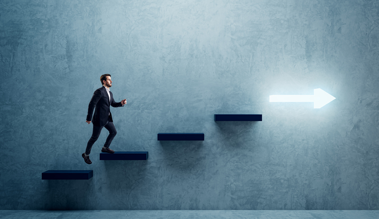 Side view of young business man climbing illuminated arrow stairs to success on concrete wall background in interior. Financial growth, career development and forward concept