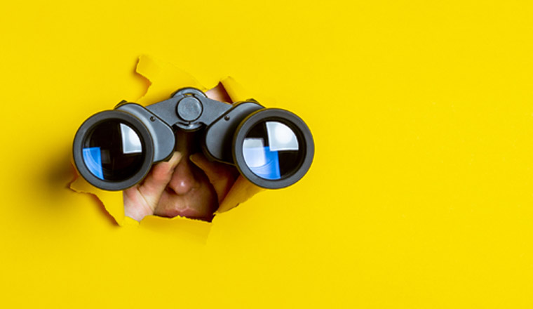 Female hand holds black binoculars on a yellow background. Journey, find and search concept. Banner