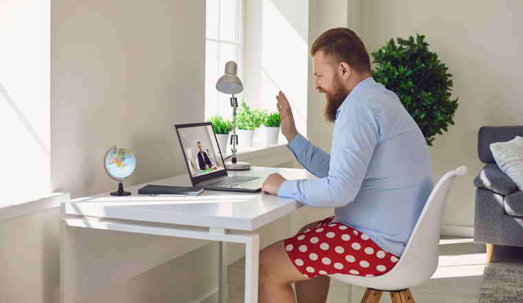 Online work at home. Funny man in red shorts works communicates using laptop sitting at the table at the workplace at home office in the room.