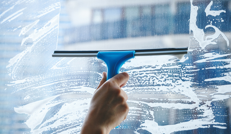 young female hand cleaning dirty glass window with a squeegee