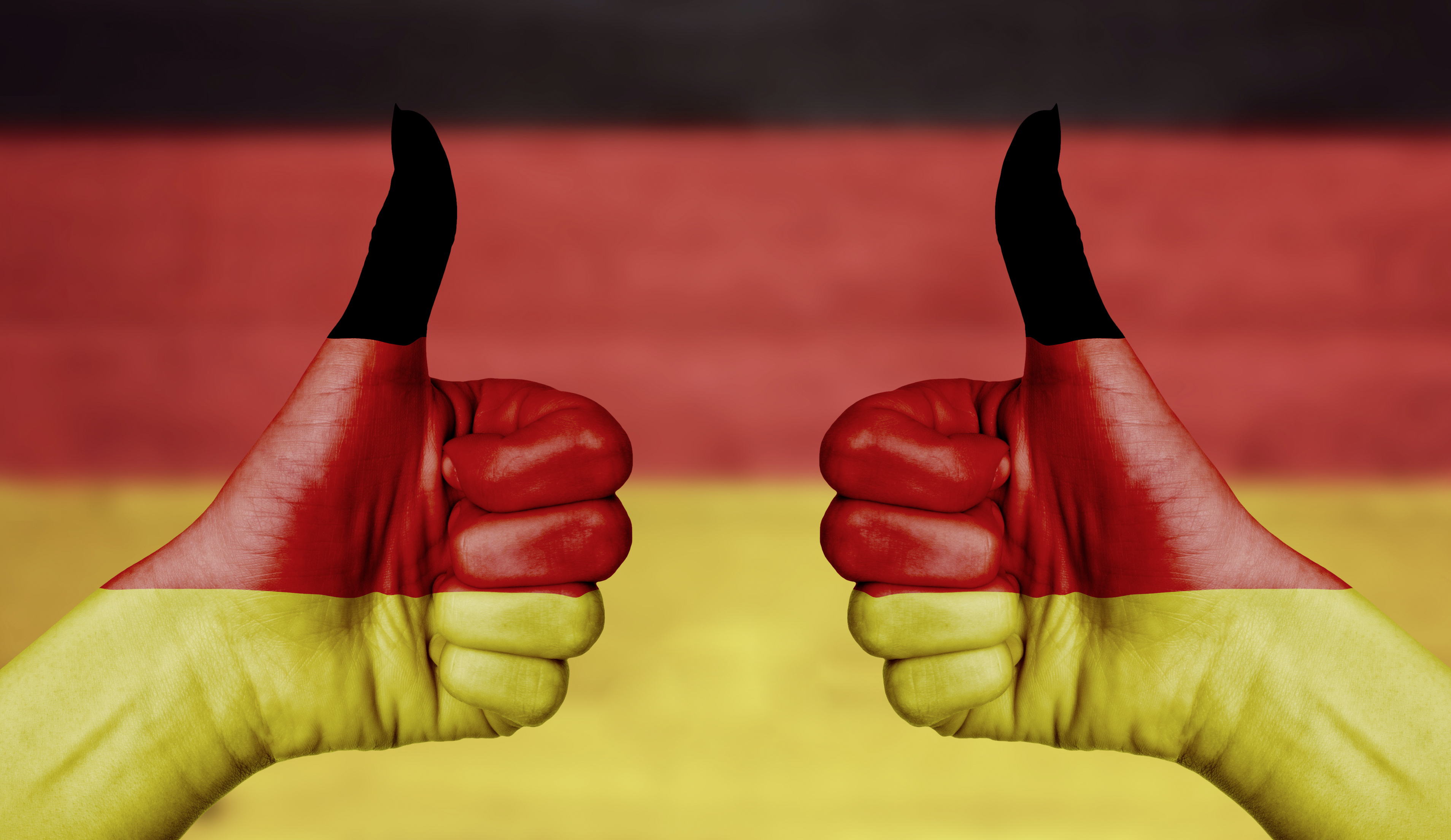 Germany flag painted on female hands thumbs up with blurry wooden background
