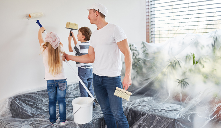 Kinder streichen Wand mit Hilfe vom Vater bei der Renovierung im Eigenheim