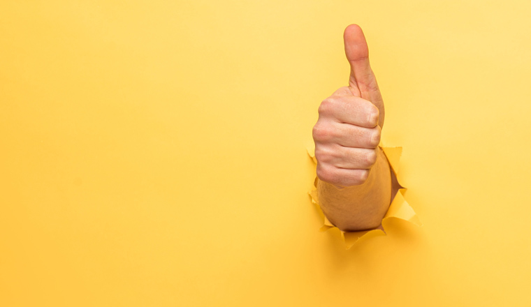 cropped view of man showing thumb up through yellow paper hole, panoramic shot