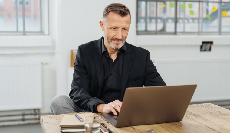Businessman sitting working at a laptop computer in a large office typing information with a look of concentration