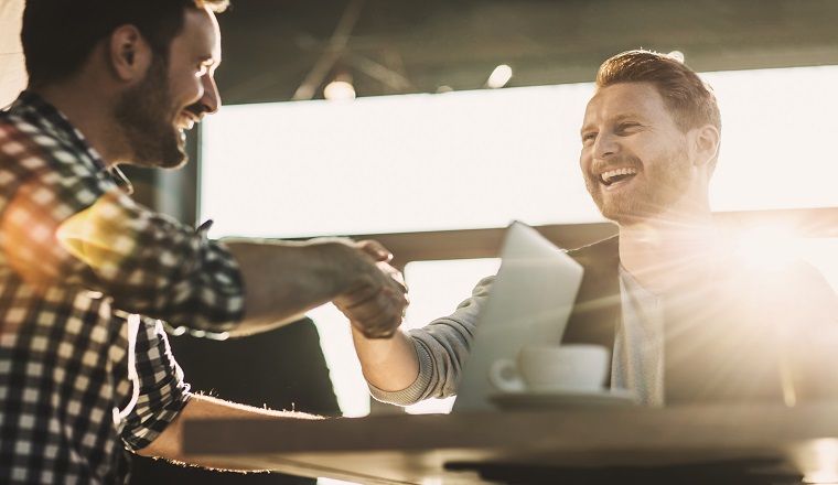 Happy red-haired businessman shaking hands with his colleague in a cafe. Focus is on redhead man.