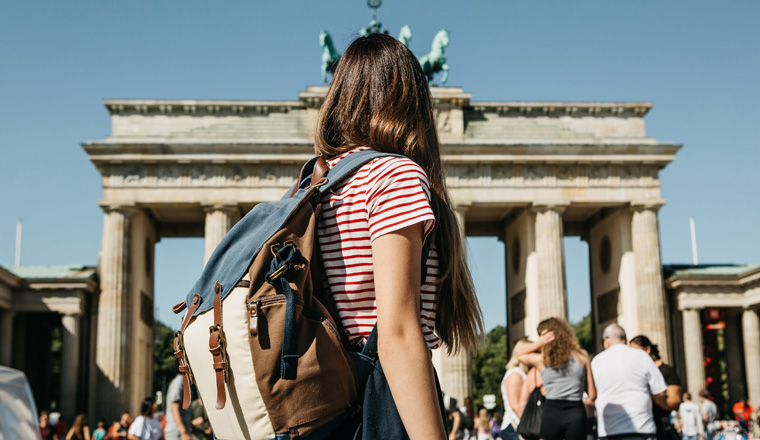 A tourist or a student with a backpack in Berlin in Germany visits the sights. Ahead is the Brandenburg Gate and unrecognizable blurred people.